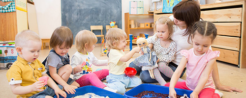 Gruppe von Kindern mit Erzieherin sitzen auf dem Boden und spielen