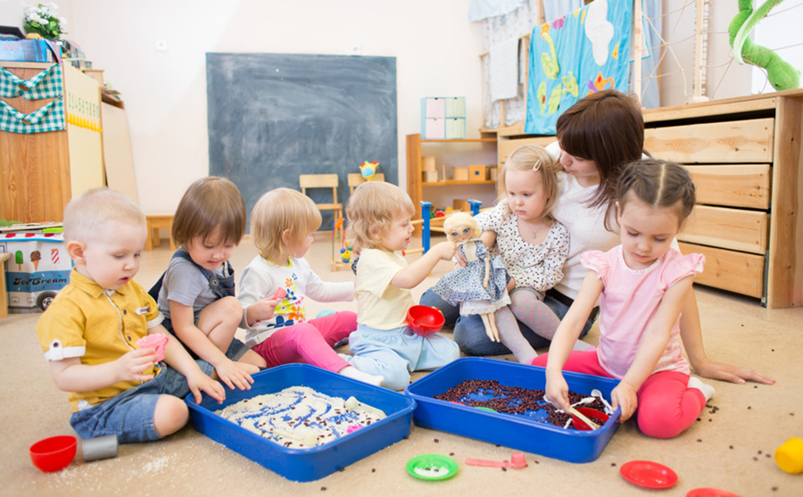 Gruppe von Kindern mit Erzieherin sitzen auf dem Boden und spielen