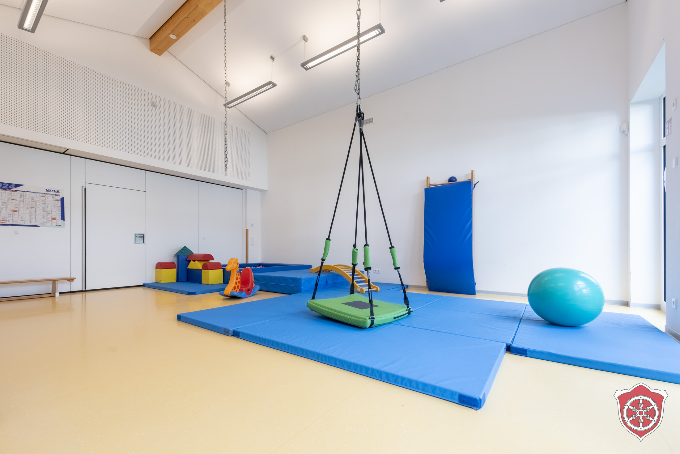 Im Turnraum sind Turnmattten auf dem Boden. Ein großer Gymnastikball liegt auf einer der Matten. Mittig hängt von der Decke eine große Korbschaukel.