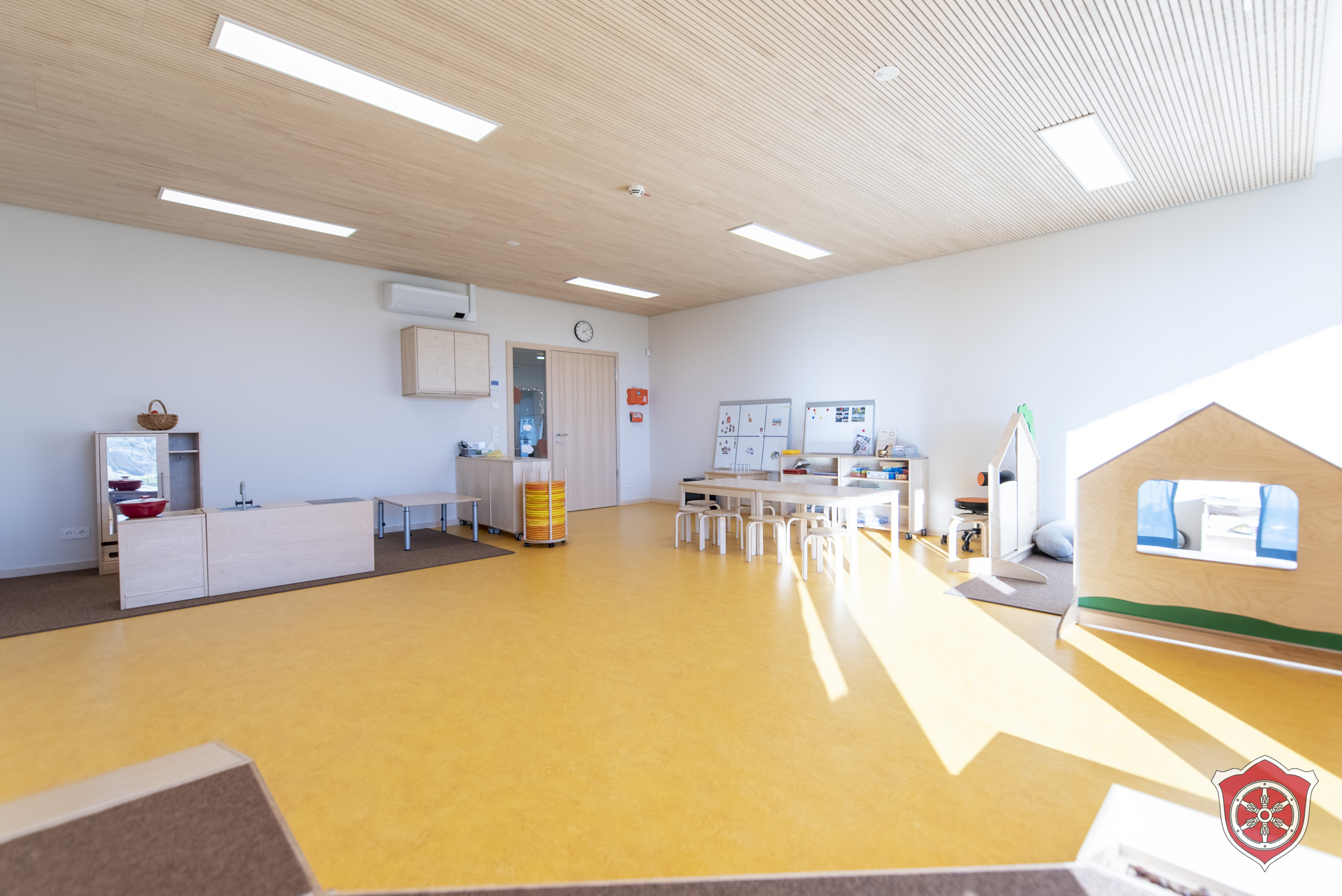 Der Ü3 Gruppenraum ist in die verschiedenen Bereiche eingeteilt. Es ist eine Rollenspielecke und eine TIschgruppe zu sehen.