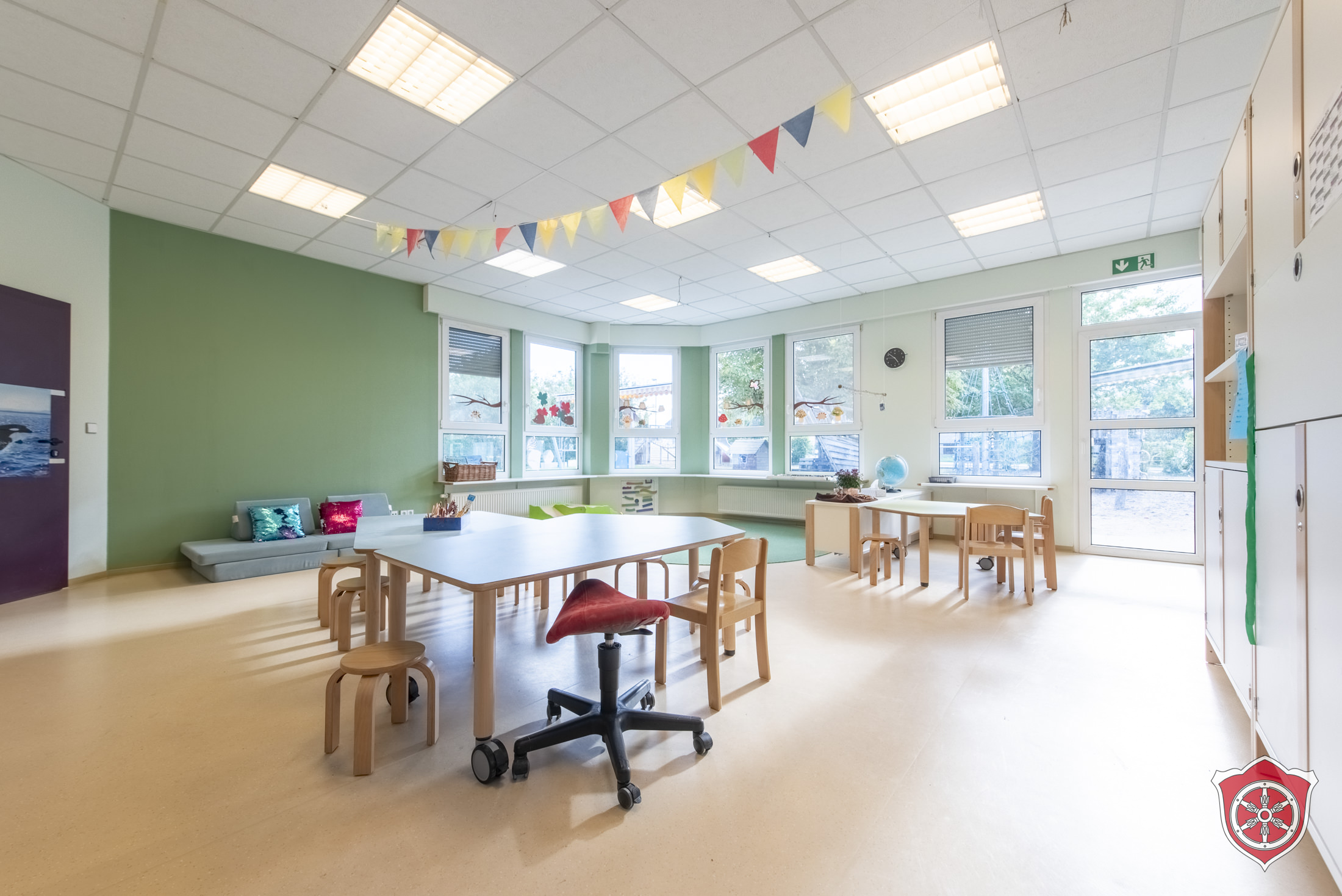 Gruppenraum mit kleiner Kuschelecke und zwei Tischgruppen mit Stühlen.