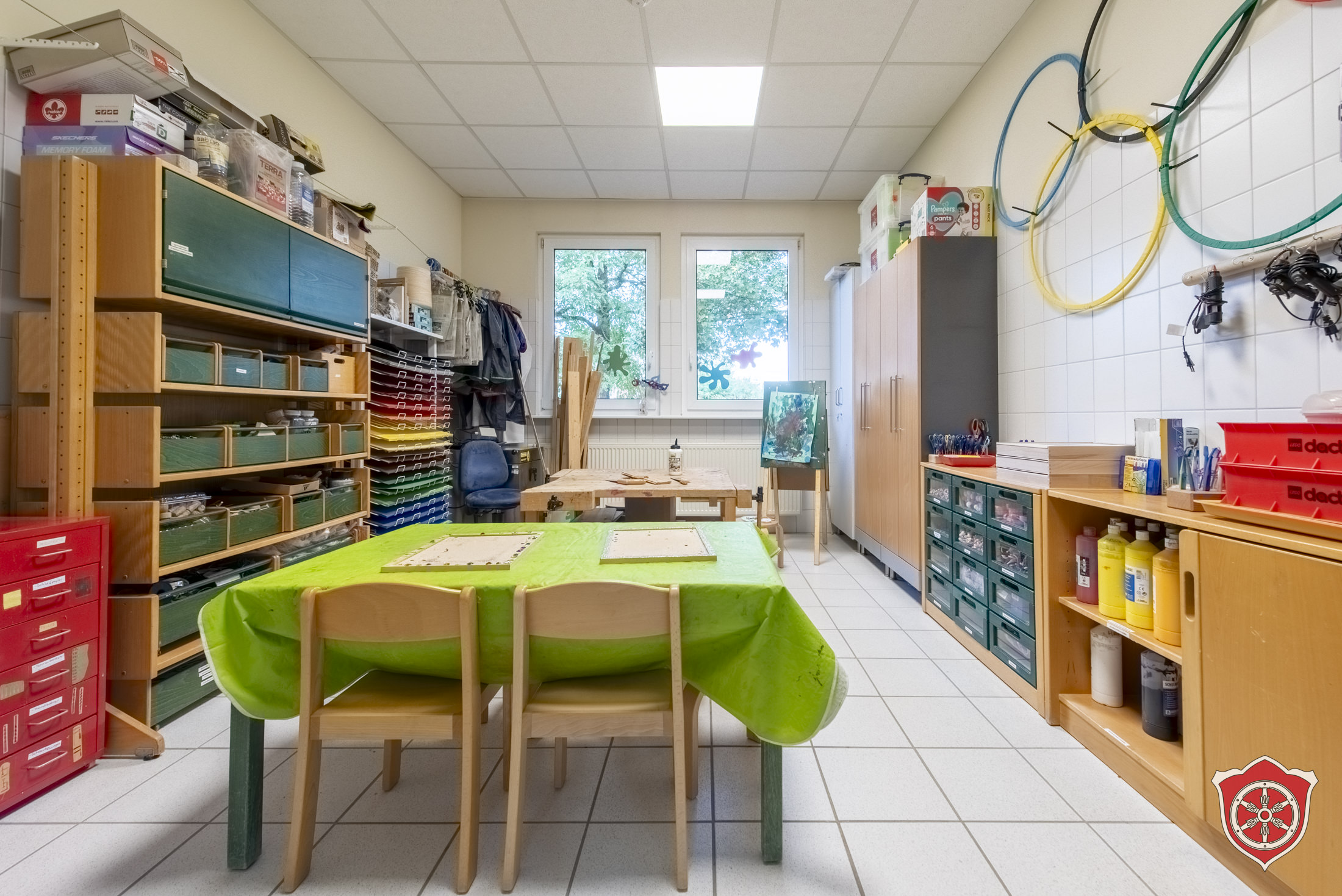 Im Werkräum sind Regale und Schränke mit vielen Materialien. In der Mitte des Bildes sind Werkbänke.